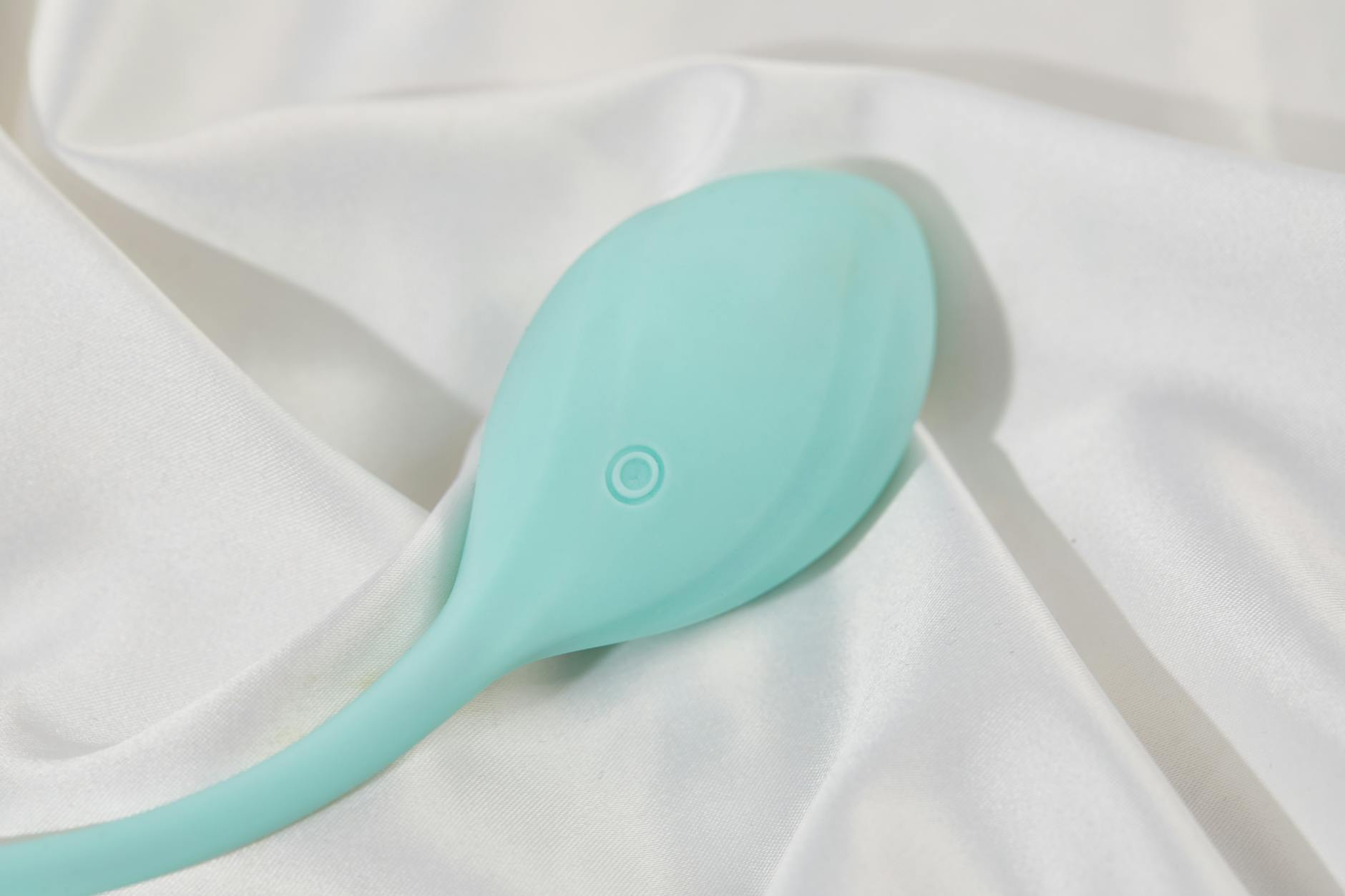 A sleek teal clitoral vibrator displayed on soft white silk