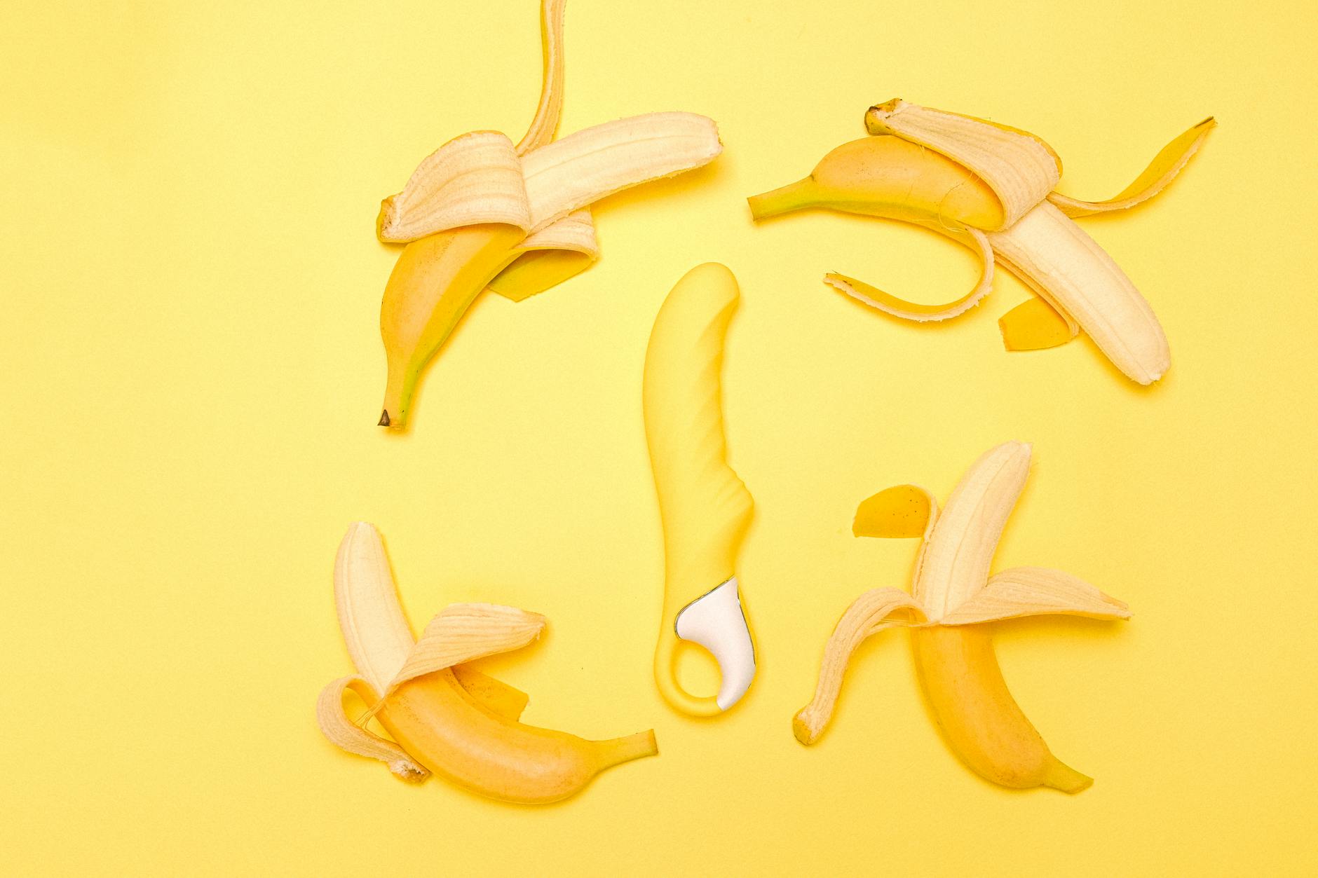 Yellow silicone lemon vibrator surrounded by fresh lemons and bananas on a bright yellow background