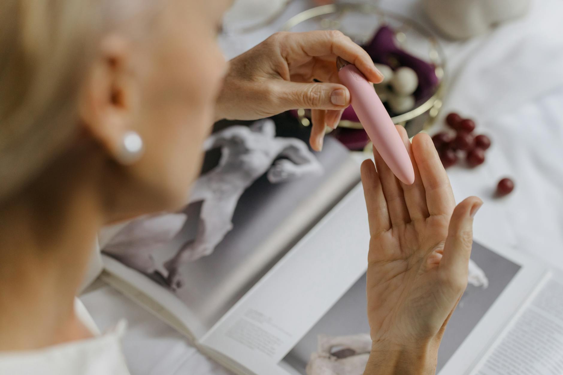 Close-up of a woman holding a pink vibrator with art books nearby, emphasizing intimate sensuality and personal connection.